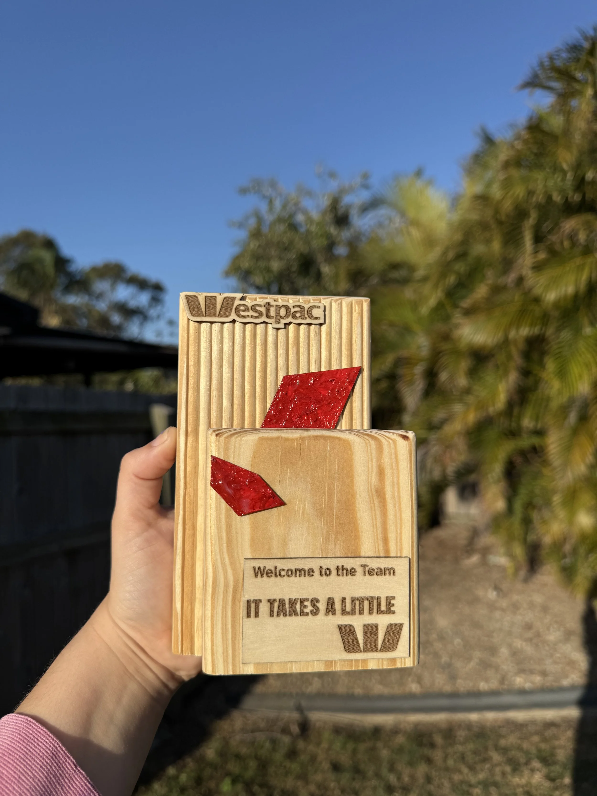 Westpac 'Welcome to the Team' trophy in reclaimed timber with a red diamond inlay, held up in a sunny backyard.