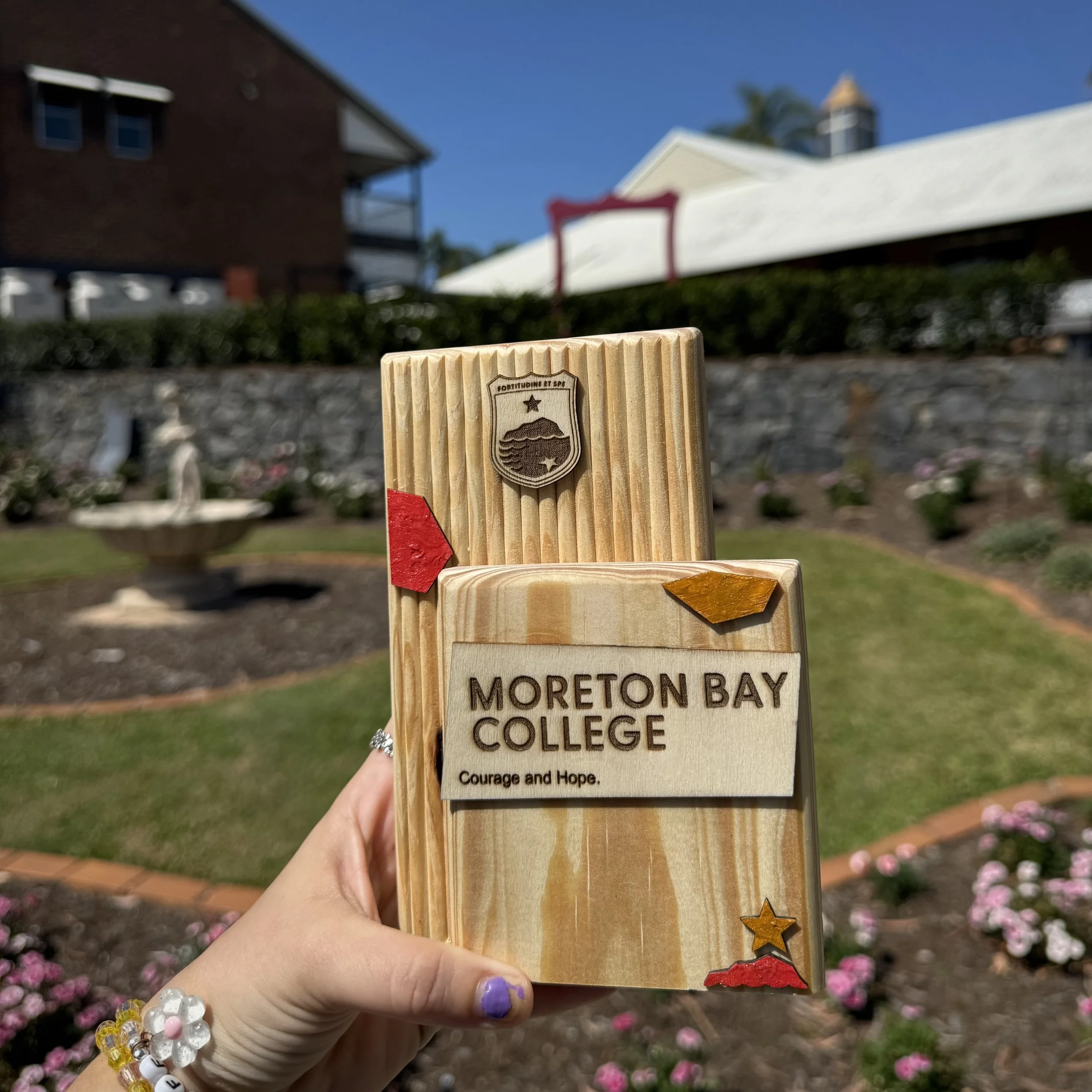 Moreton Bay College trophy reading 'Courage and Hope' with the school crest, held in a rose garden.