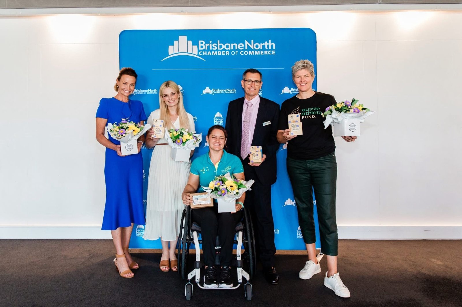 Five honourees with their Bloom Cycle awards and flower boxes in front of a Brisbane North Chamber of Commerce backdrop.