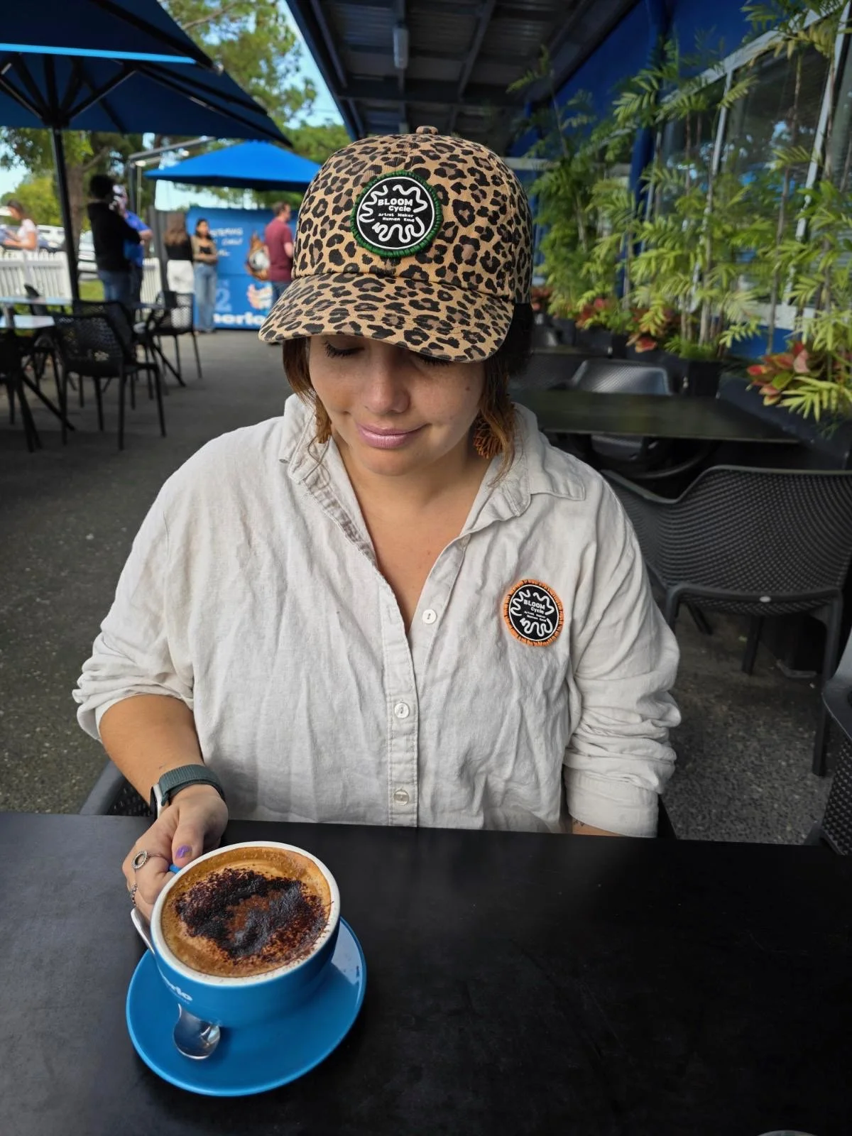 Zoe in a Bloom Cycle leopard-print cap, taking notes over coffee.