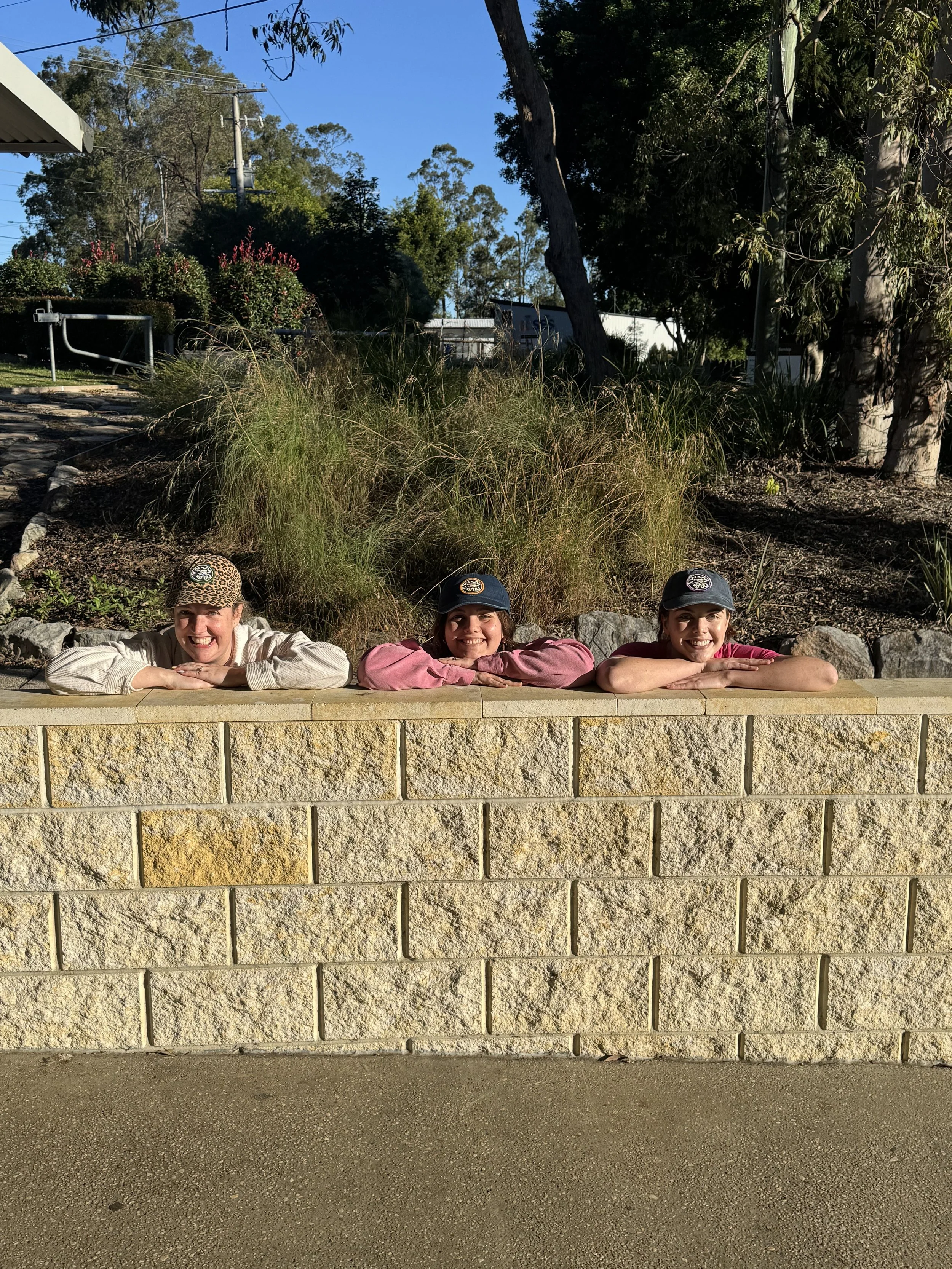 Three Bloom Cycle team members peeking over a sandstone wall with native plants behind them.