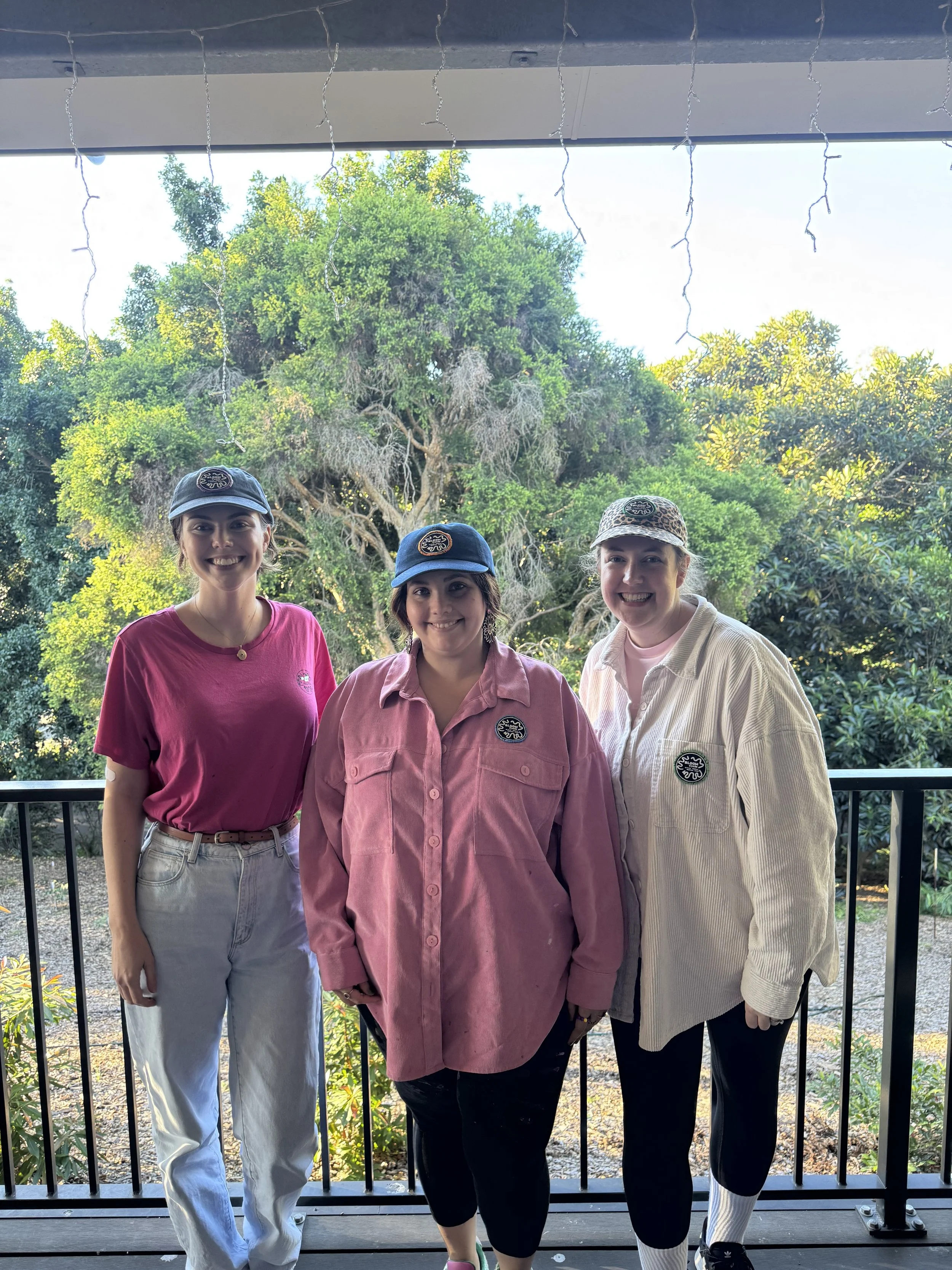 Three Bloom Cycle team members on a deck wearing branded caps.