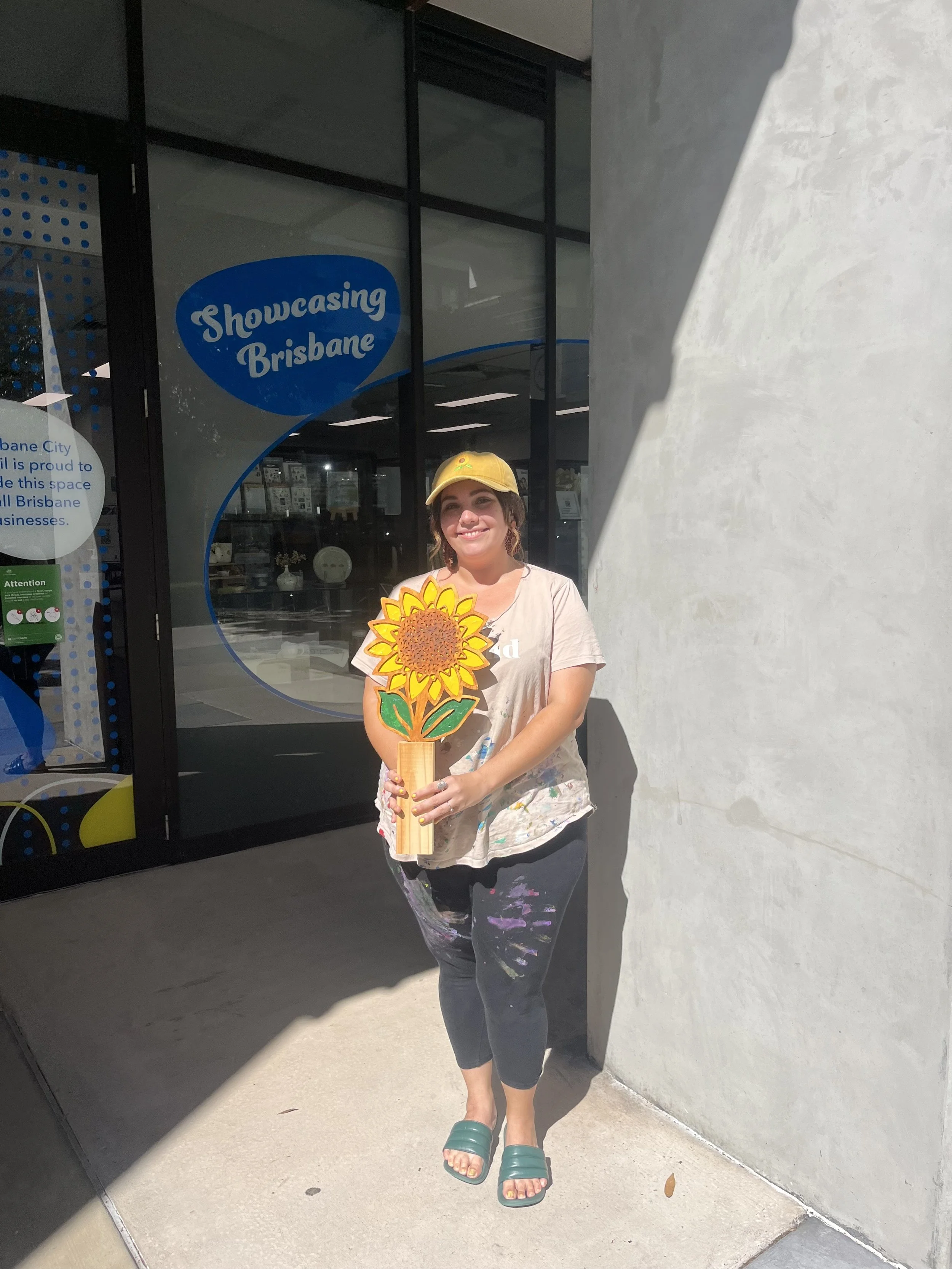 Zoe holding a sunflower-topped trophy outside a Brisbane City Council Showcasing Brisbane window display.
